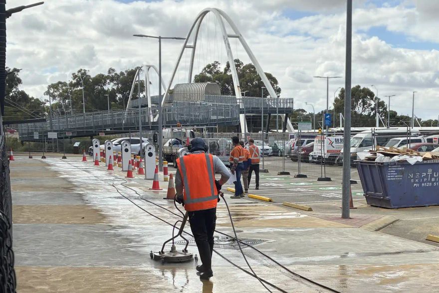 Michael wearing high-vis clothing while pressure cleaning paving at a train-station worksite.