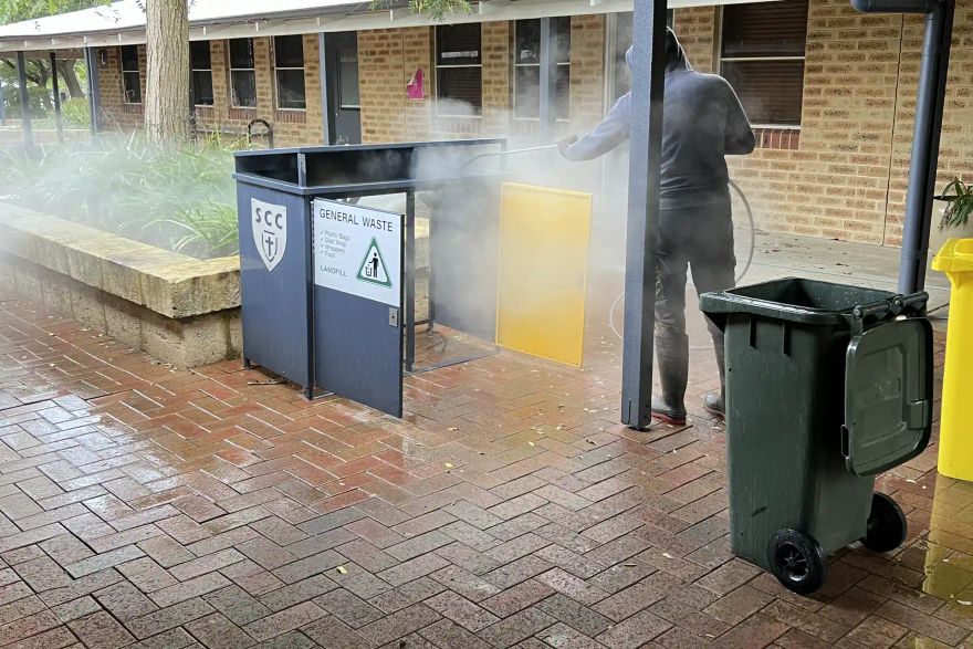 Michael pressure cleaning a bin enclosure in a school courtyard.